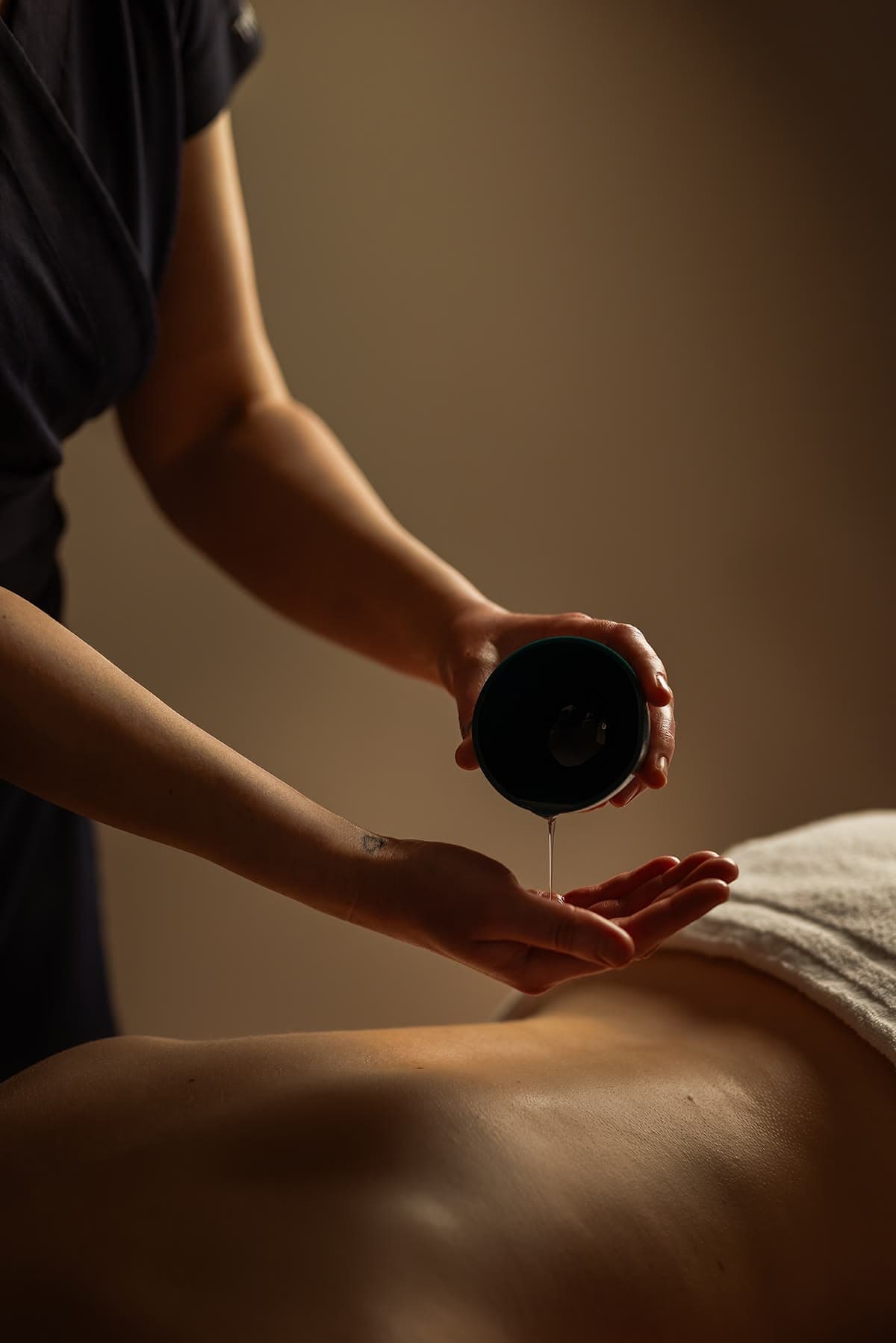 Terapeuta preparando óleo de massagem na palma da mão, atendimento profissional com luz suave